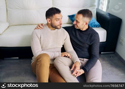 Gay couple sitting near the couch at home in a romantic moment. Homosexual relationship concept.. Gay couple sitting near the couch at home in a romantic moment