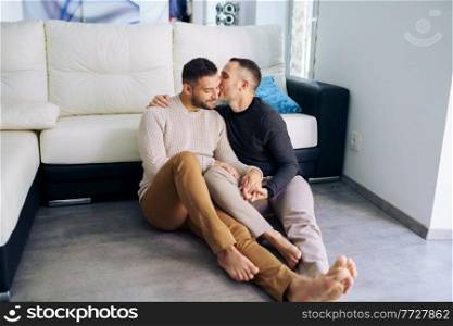 Gay couple sitting near the couch at home in a romantic moment. Homosexual relationship concept.. Gay couple sitting near the couch at home in a romantic moment