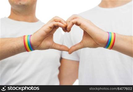 gay couple with rainbow wristbands and hand heart. lgbt, same-sex love and homosexual relationships concept - close up of happy male couple wearing gay pride rainbow awareness wristbands showing hand heart gesture