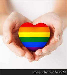 gay pride, homosexual, love and charity concept - close up of female hands holding small rainbow heart