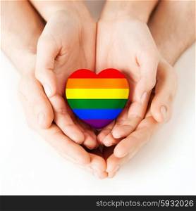 gay pride, homosexual, love and charity concept - close up of male and female hands holding small rainbow heart