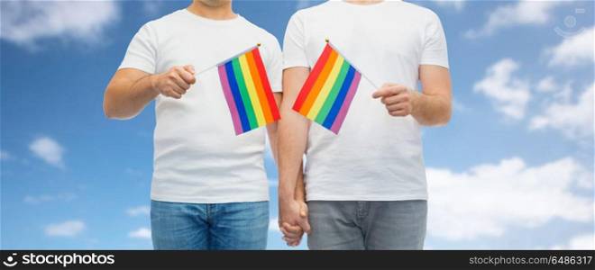 gay pride, lgbt and homosexual concept - close up of happy male couple with rainbow flags in white t-shirts holding hands over blue sky and clouds background. male couple with gay pride flags holding hands. male couple with gay pride flags holding hands