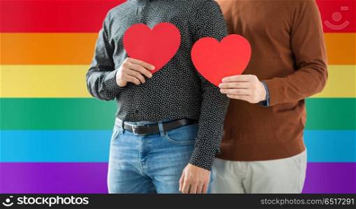 gay pride, lgbt and homosexual concept - close up of happy male couple holding red hearts over rainbow colors background. close up of happy male couple holding red hearts. close up of happy male couple holding red hearts
