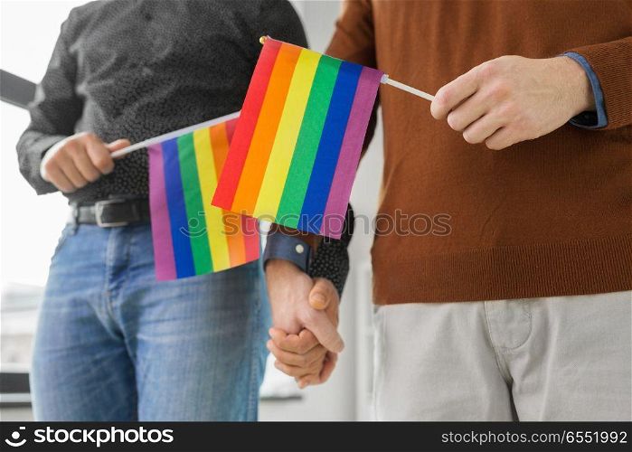 gay pride, lgbt and homosexual concept - close up of happy male couple with rainbow flags holding hands. male couple with gay pride flags holding hands. male couple with gay pride flags holding hands