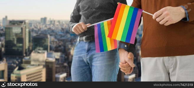 gay pride, lgbt and homosexual concept - close up of happy male couple with rainbow flags holding hands over tokyo city background. male couple with gay pride flags holding hands