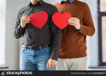 gay pride, lgbt and homosexual concept - close up of happy male couple holding red hearts. close up of happy male couple holding red hearts. close up of happy male couple holding red hearts