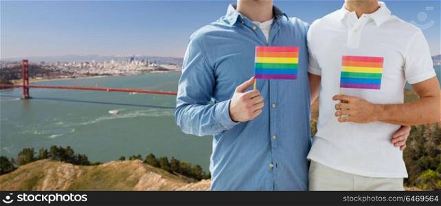 gay pride, lgbt and homosexual relationships concept - close up of happy male couple with rainbow flags hugging over golden gate bridge in san francisco bay background. men with gay pride flags over golden gate bridge