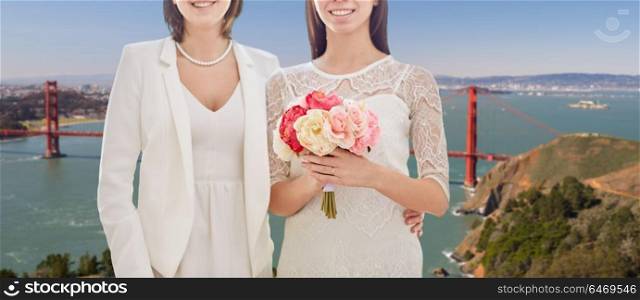gay, same-sex marriage and homosexual relationships concept - close up of happy married lesbian couple with flower bunch over golden gate bridge in san francisco bay background. female gay couple wedding over golden gate bridge