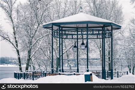 Gazebo with wooden benches, in the Naltalka park of Kiev, Ukraine, near the Dnieper river, during a snowy winter day
