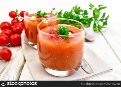 Gazpacho tomato soup in two glasses with parsley and vegetables on a napkin against the background of wooden boards