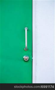 Geen door with metal handle and lock and white cement wall.