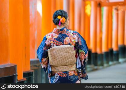 "Geishas girl wearing Japanese kimono among red wooden Tori Gate at Fushimi Inari Shrine in Kyoto, Kimono is a Japanese traditional garment. The word "kimono", which actually means a "thing to wear""