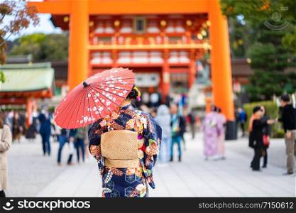 "Geishas girl wearing Japanese kimono among red wooden Tori Gate at Fushimi Inari Shrine in Kyoto, Kimono is a Japanese traditional garment. The word "kimono", which actually means a "thing to wear""