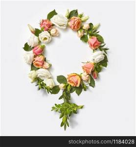 Gender symbol sign of woman craft from flowers and green twigs of plant on a light grey background, copy space. Top view.. Female gender symbol from flowers.