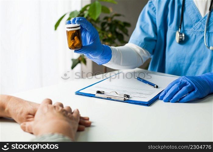 General Practitioner UK GP doctor holding bottle of prescription drugs,handing over to patient during medical check up,healthcare professional prescribing treatment therapy to elderly senior citizen