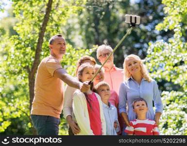 generation and people concept - happy family taking picture with smartphone and selfie stick in summer garden. happy family taking selfie in summer garden