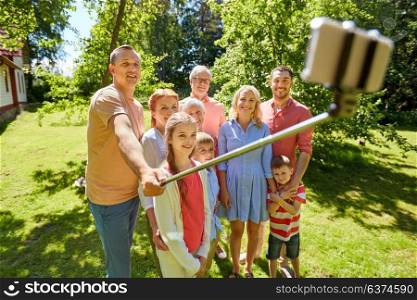 generation, technology and people concept - happy family taking picture with smartphone and selfie stick in summer garden. happy family taking selfie in summer garden