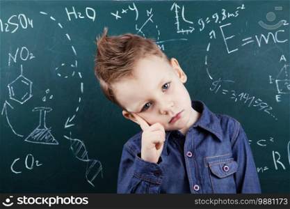 Genius boy near blackboard with formulas. Funny portrait clever pupil boy on school board background. Back to school