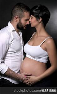 Gentle couple awaiting baby, beautiful pregnant woman with husband over black background, happy anticipation of new life