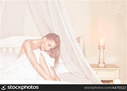 Gentle girl enjoying wonderful day in luxury spa hotel, sitting on the bed under white transparent net and thoughtful looking down &#xA;