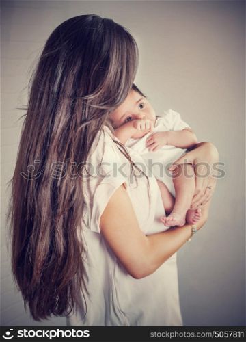 Gentle mother with little baby isolated on gray background, woman with dark long hair holding her precious newborn daughter, love and happy motherhood concept