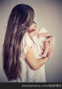 Gentle mother with little baby isolated on gray background, woman with dark long hair holding her precious newborn daughter, love and happy motherhood concept