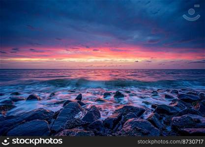 Gentle sunset on the sea coast. Stunning view of waves crashing on rock formations under pastel skies at West Kapelle, Zeeland, Netherlands. Breathtaking sunset with pastel colors and smooth white water along rocky dutch coast