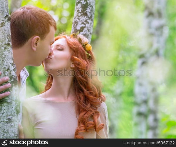 Gentle young happy couple kissing in the park, standing between two beautiful birch tree, celebrate wedding day, love and togetherness concept