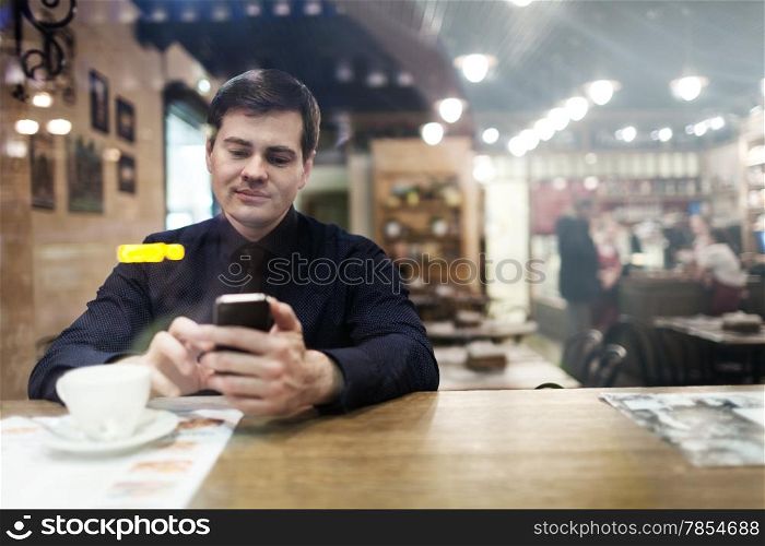 Gentleman sitting at the table using his phone texting and drinking coffee