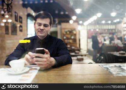 Gentleman sitting at the table using his phone texting and drinking coffee