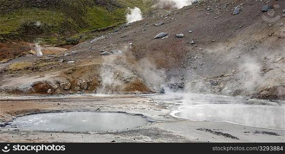 Geothermal water ponds steaming next to rocky slope
