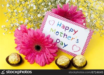 Gerbera daisies and mothers day card on yellow background