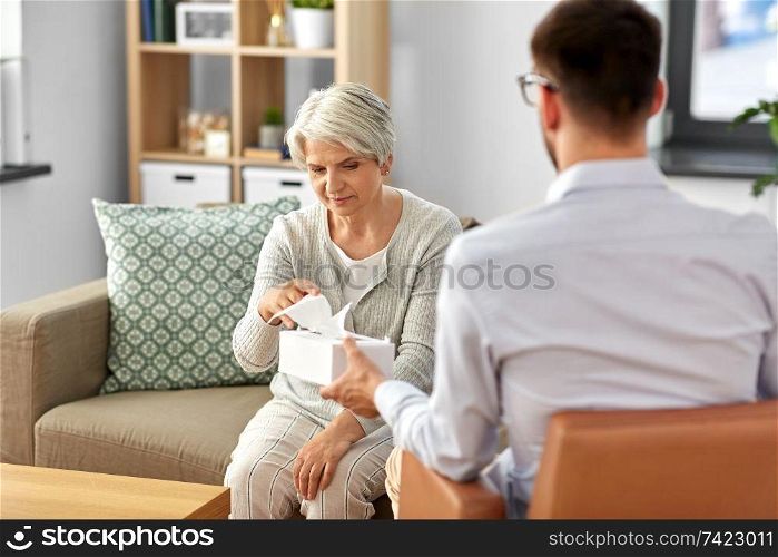 geriatric psychology, mental therapy and old age concept - psychologist giving tissues to sad unhappy senior woman client at psychotherapy session. psychologist giving tissues to senior woman client