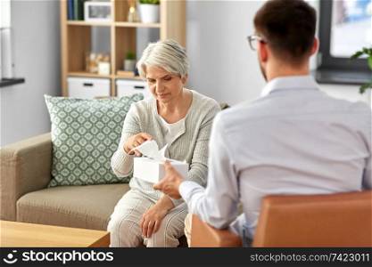 geriatric psychology, mental therapy and old age concept - psychologist giving tissues to sad unhappy senior woman client at psychotherapy session. psychologist giving tissues to senior woman client
