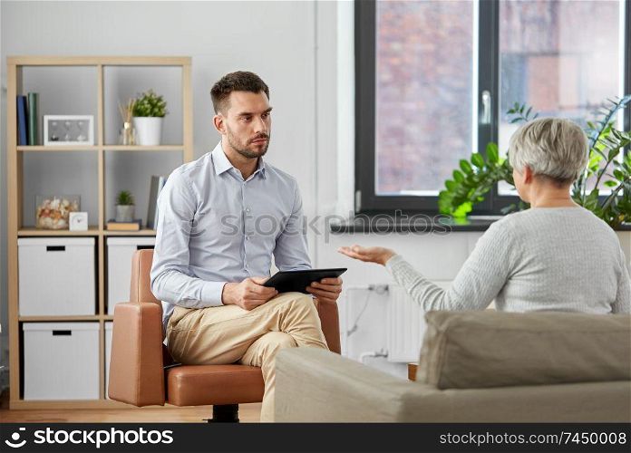 geriatric psychology, mental therapy and old age concept - psychologist with tablet computer listening to senior woman patient at psychotherapy session. psychologist listening to senior woman patient