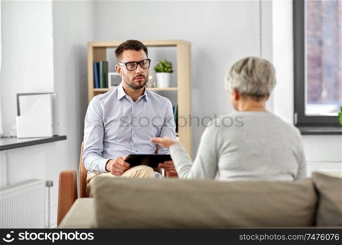 geriatric psychology, mental therapy and old age concept - psychologist with tablet computer listening to senior woman patient at psychotherapy session. psychologist listening to senior woman patient