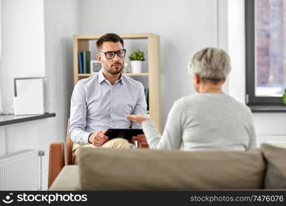 geriatric psychology, mental therapy and old age concept - psychologist with tablet computer listening to senior woman patient at psychotherapy session. psychologist listening to senior woman patient