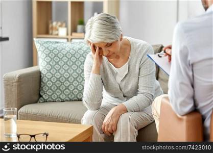 geriatric psychology, mental therapy and old age concept - sad unhappy senior woman patient and psychologist with clipboard taking notes at psychotherapy session. sad senior woman patient and psychologist