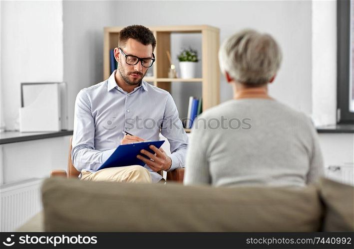 geriatric psychology, mental therapy and old age concept - senior woman patient and psychologist with clipboard taking notes at psychotherapy session. senior woman patient and psychologist