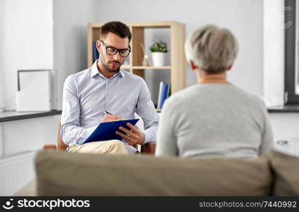 geriatric psychology, mental therapy and old age concept - senior woman patient and psychologist with clipboard taking notes at psychotherapy session. senior woman patient and psychologist