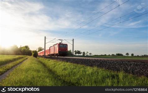 German red train traveling through nature, on a summer sunny day, at sunset, near Schwabisch Hall, Germany. Railroad tracks through agriculture field.