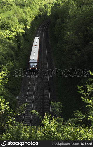 German regional train traveling on railway surrounded by trees and green nature, near Schwabisch Hall, Germany, on a sunny day of summer. Railroad.