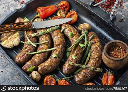 German sausages with grilled mushrooms and tomatoes.Grill pan with delicious grilled sausages. Grilled sausages in frying pan