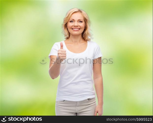 gesture, advertisement and people concept - smiling middle aged woman in blank white t-shirt showing thumbs up over green natural background