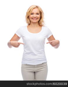 gesture, advertisement and people concept - smiling middle aged woman in blank white t-shirt pointing finger to herself