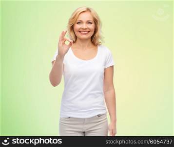 gesture, advertisement and people concept - smiling woman in blank white t-shirt showing ok hand sign over green natural background