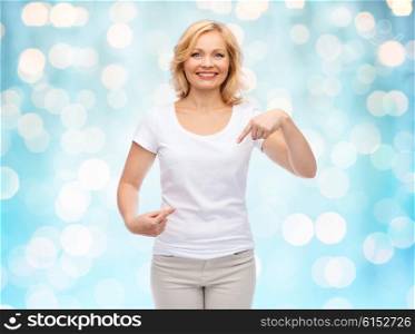 gesture, advertisement and people concept - smiling woman in blank white t-shirt pointing finger to herself over blue holidays lights background