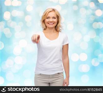 gesture, advertisement and people concept - smiling woman in blank white t-shirt pointing finger to you over blue holidays lights background