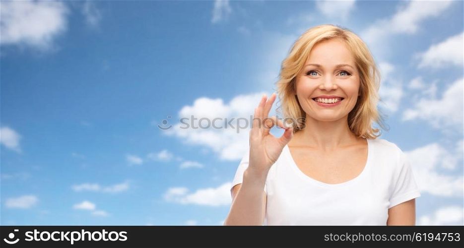 gesture, advertisement and people concept - smiling woman in blank white t-shirt showing ok hand sign over blue sky and clouds background