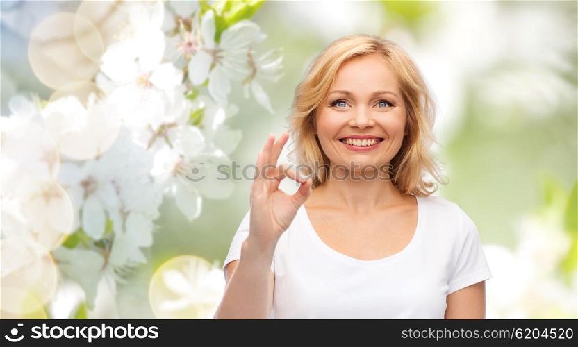 gesture, advertisement and people concept - smiling woman in blank white t-shirt showing ok hand sign over natural spring cherry blossom background